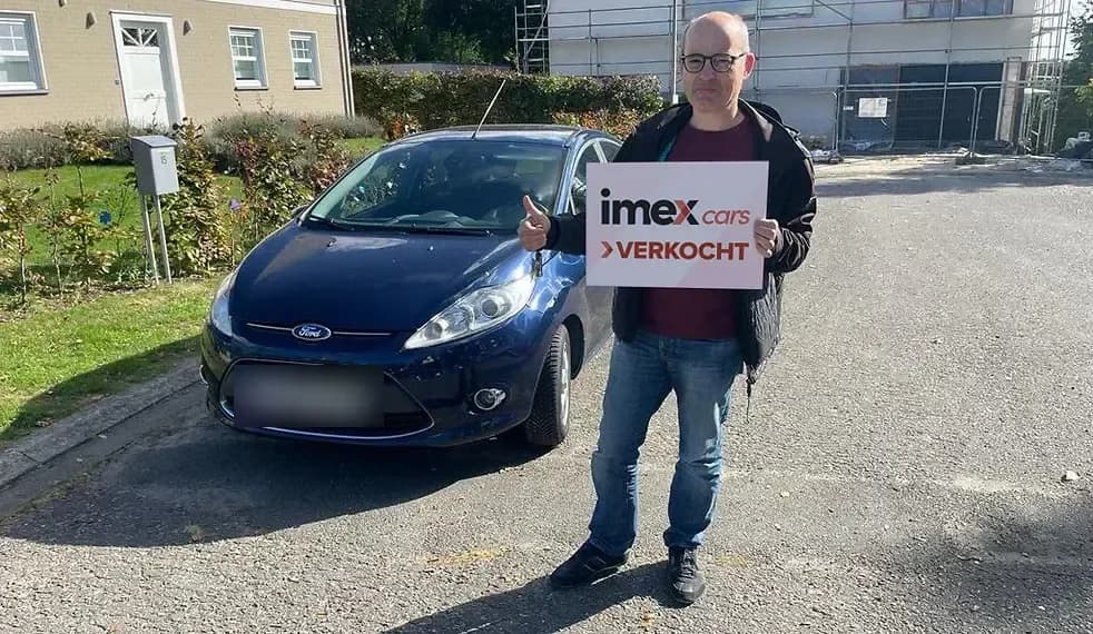 Verkoper met Imex Cars ‘VERKOCHT’ bord naast verkochte Ford, verkoop je auto in België