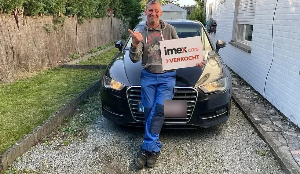 Lachende verkoper met Imex Cars ‘VERKOCHT’ bord bij verkochte auto, verkoop je auto in België