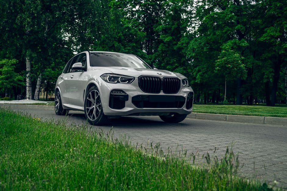 Witte BMW-SUV van schuin voren op een weg langs bomen
