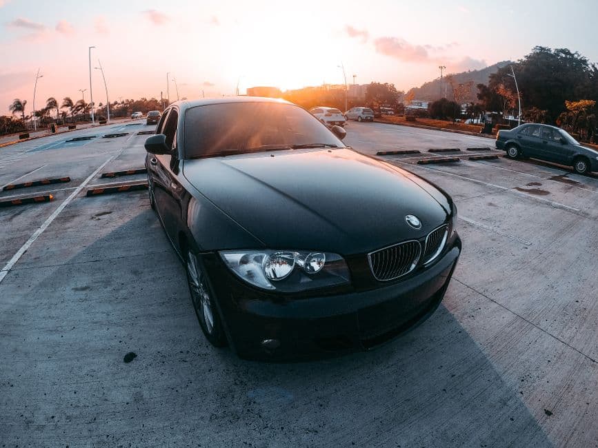 Zwarte BMW van schuin voren op een ruime parking met de zon laag aan de horizon