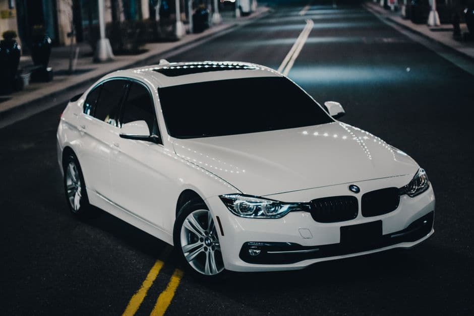 Witte BMW-sedan van schuin voren op een straat bij avond