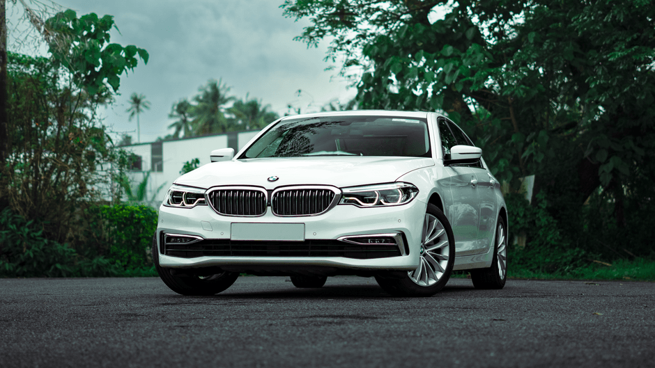 Witte BMW-sedan van voren op donker asfalt met palmbomen erachter