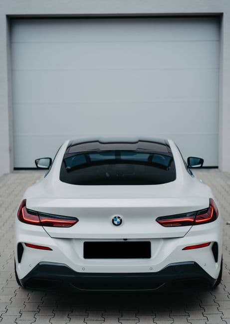 Witte BMW-coupé van achteren voor een grijze garagepoort