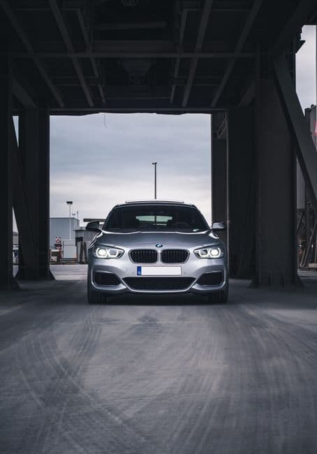 Zilvergrijze BMW recht van voren onder een stalen brug