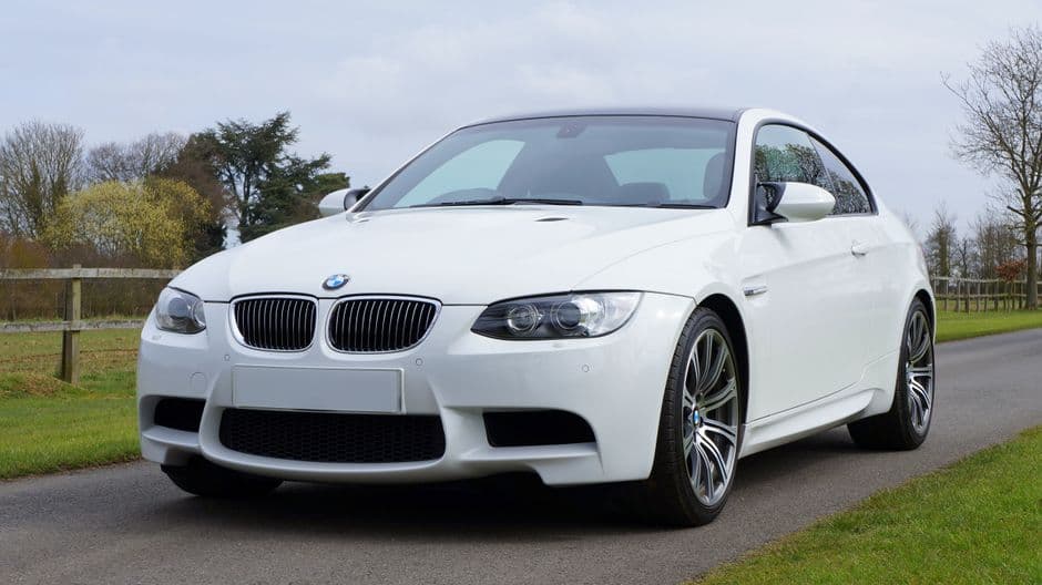 Witte BMW-coupé van schuin voren op een landweg tussen het gras