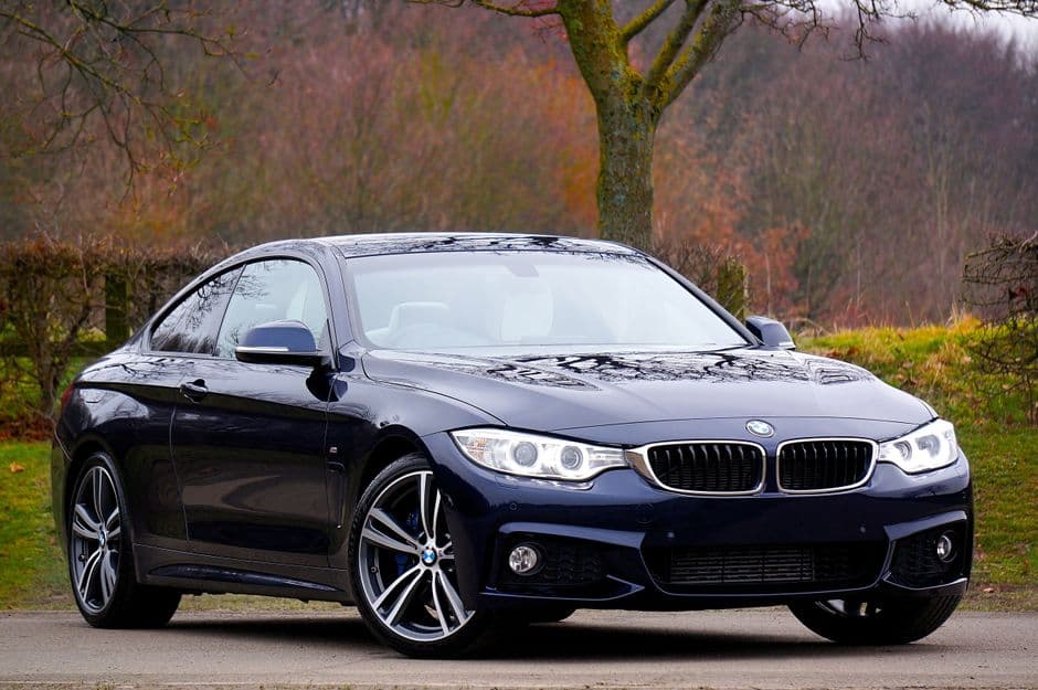 Donkerblauwe BMW-coupé van schuin voren in een herfstlandschap