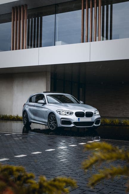 Zilvergrijze BMW-hatchback voor een modern gebouw op natte klinkers