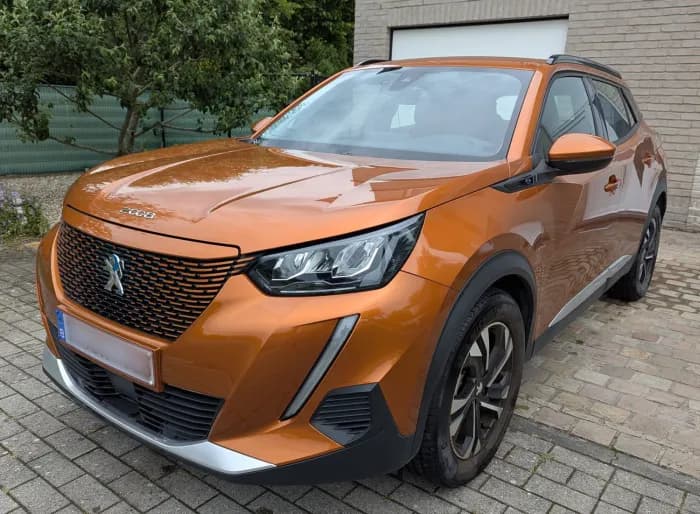 Oranje Peugeot 2008 van schuin voren op een oprit met klinkers, aangemeld bij Imex Cars