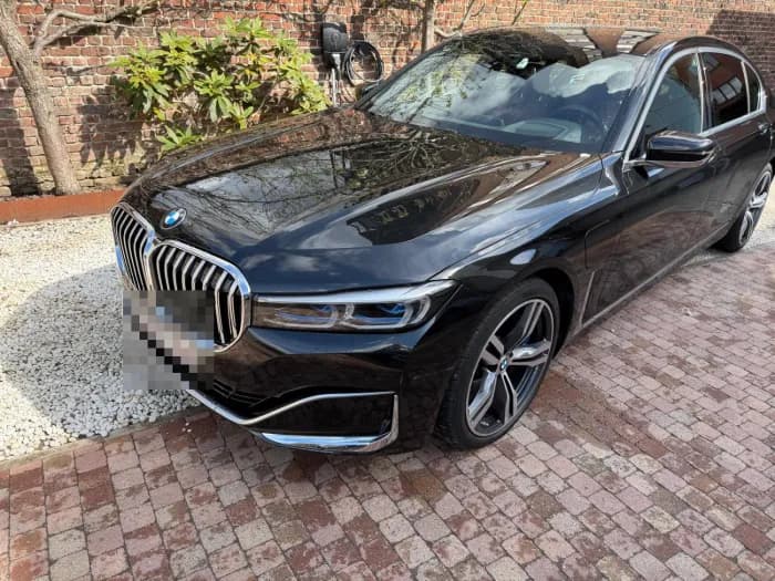 Zwarte BMW 7 Serie van schuin voren voor een bakstenen tuinmuur, aangemeld bij Imex Cars