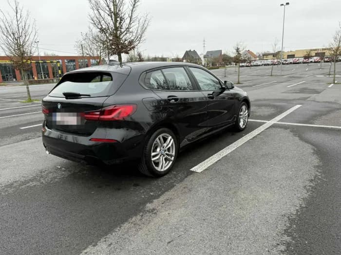 Zwarte BMW 1 Serie van schuin achteren op een grote parking, aangemeld bij Imex Cars